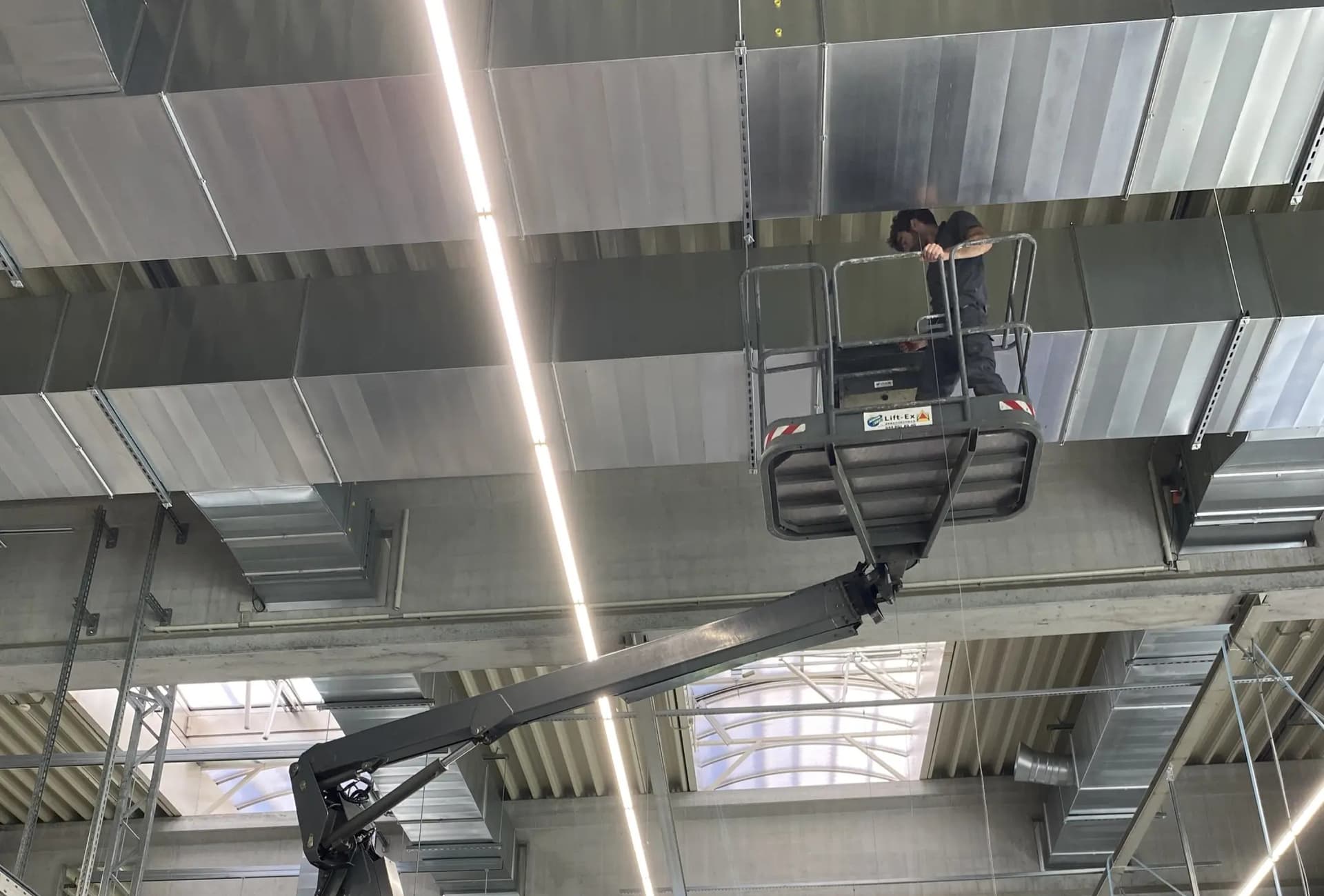 AIRnorm GmbH – Montage von Luftleitungskanälen in einer Industriehalle, Monteur auf Hebebühne bei der Installation von Stahlblechkanälen